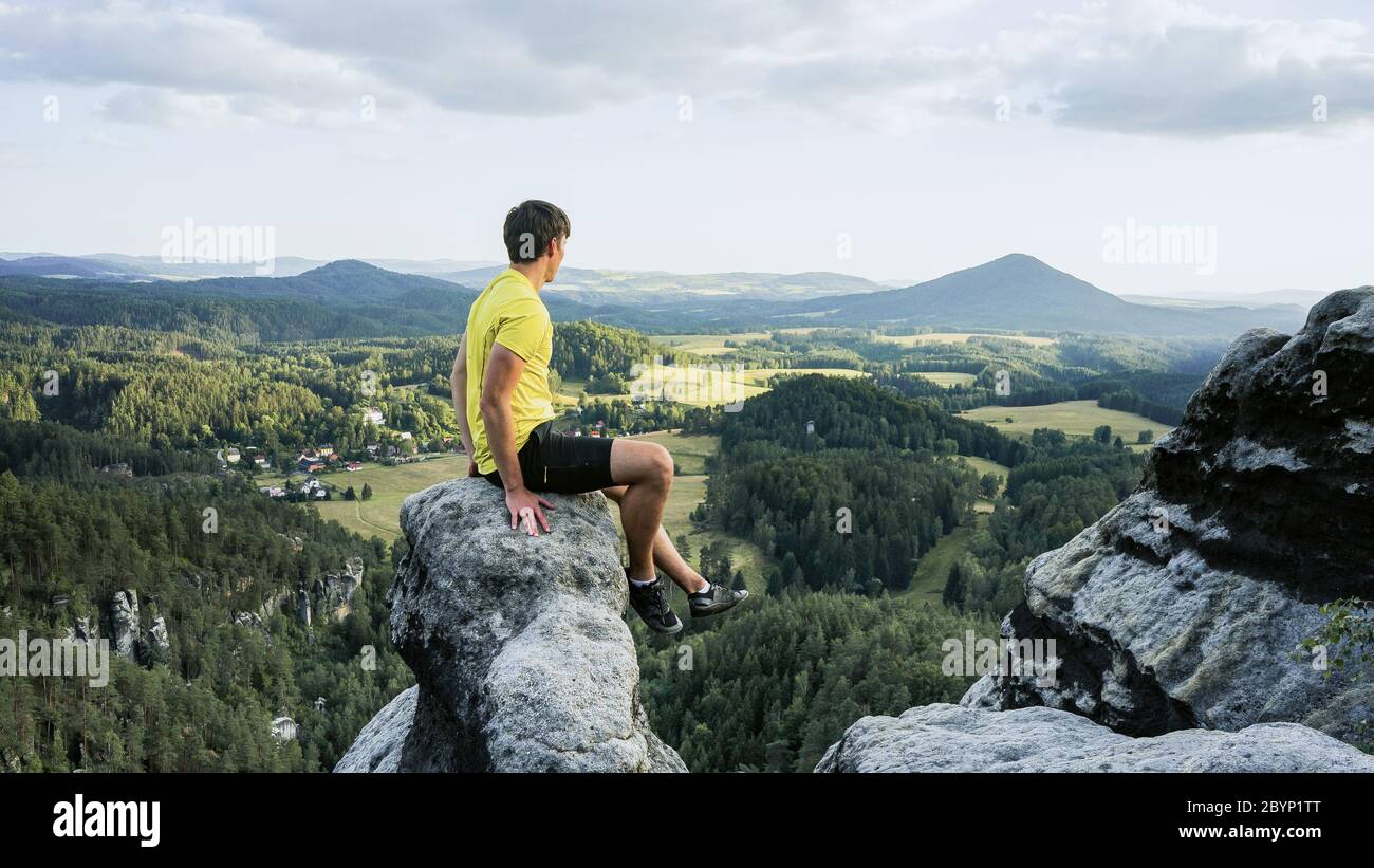 Randonneur assis sur les rochers, regardant loin et apprécier la nature. Vêtements de sport confortables. Vue depuis le mur de Vilemin jusqu'à Mary's. République tchèque Banque D'Images