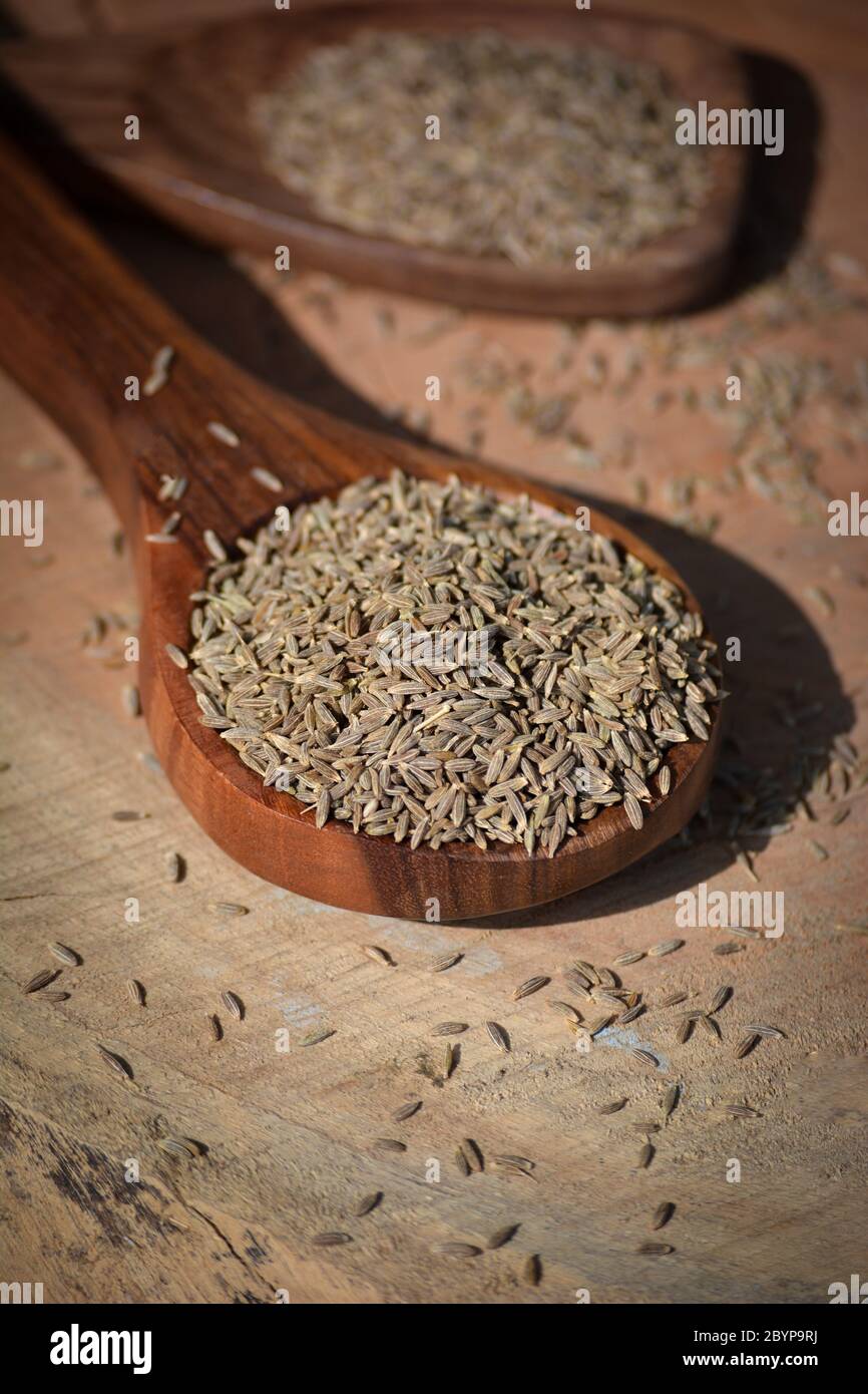 Graines de cumin en cuillère en bois sur fond en bois Banque D'Images