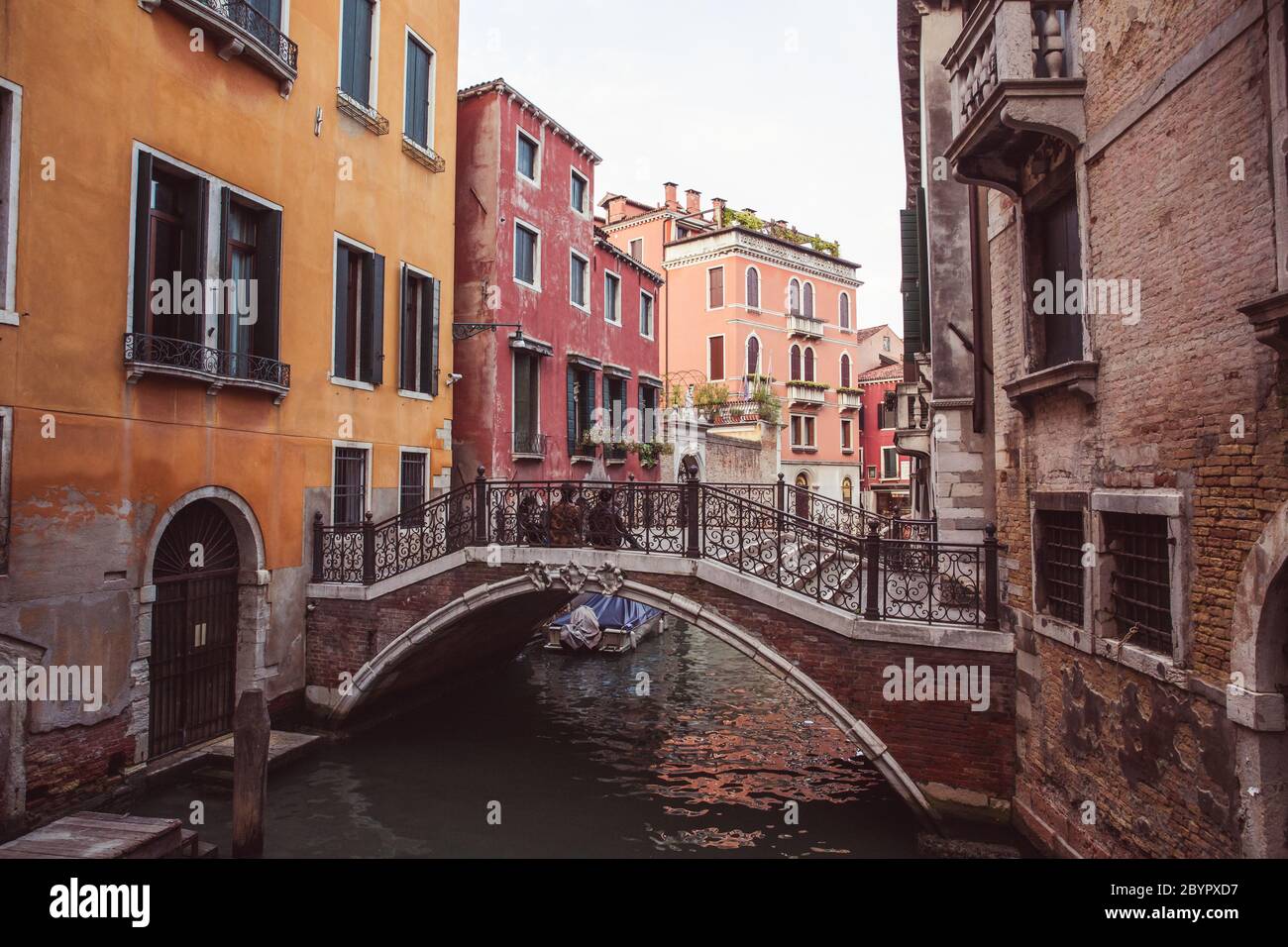 Deux amoureux assis côte à côte sur un pont au-dessus d'un canal parmi les vieux bâtiments roses et jaunes à Venise, Italie Banque D'Images