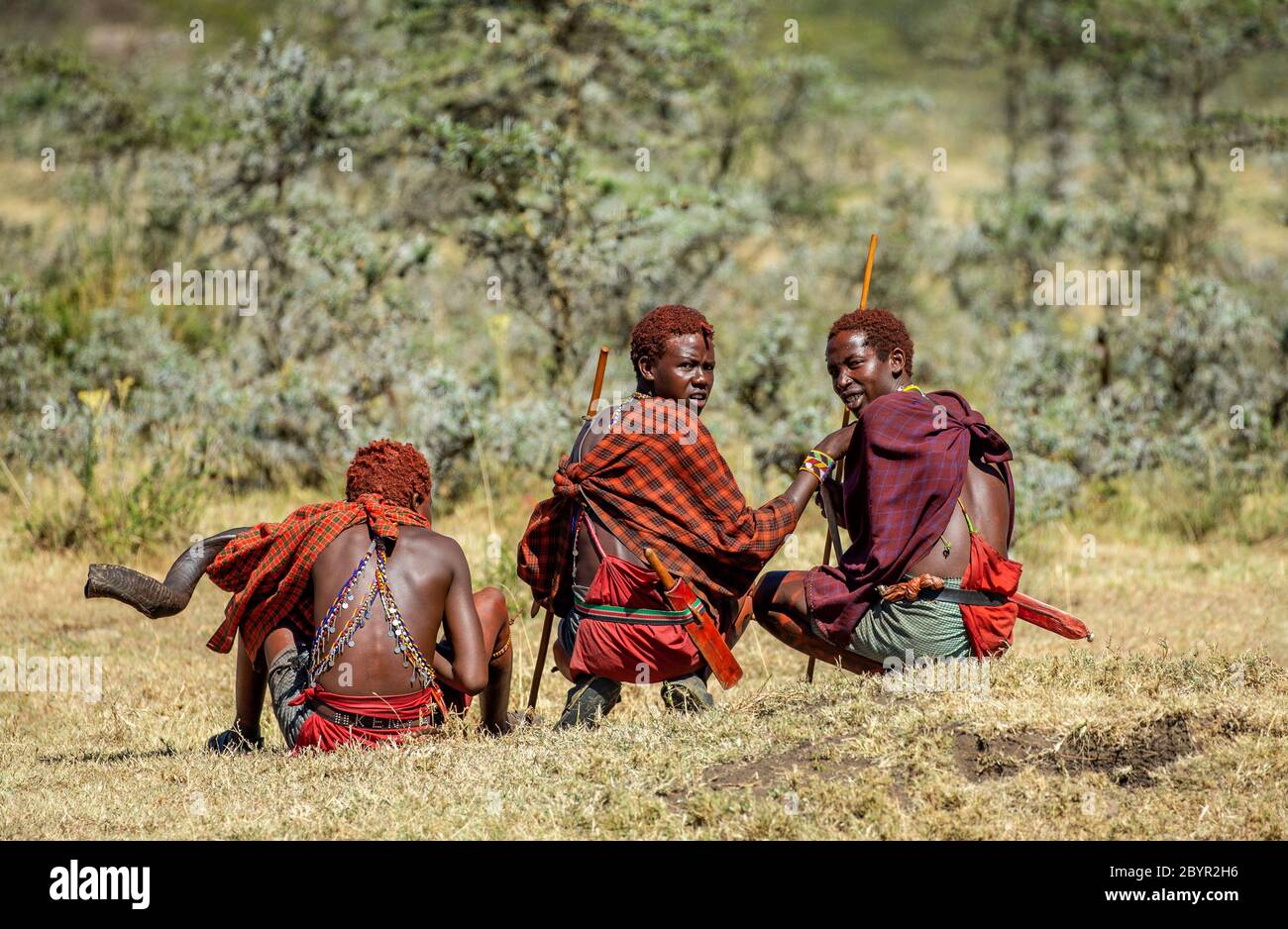 Trois jeunes guerriers Masai en vêtements et armes traditionnels sont assis dans la savane. Tanzanie, Afrique de l'est, 12 août 2018. Banque D'Images