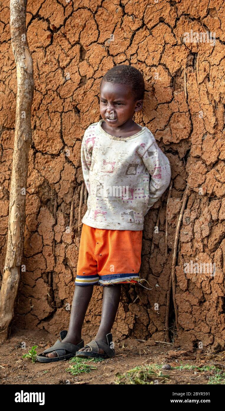 Enfant Masai sur le fond du mur d'une maison de village traditionnelle en argile. Tanzanie, Afrique de l'est, 12 août 2018. Banque D'Images