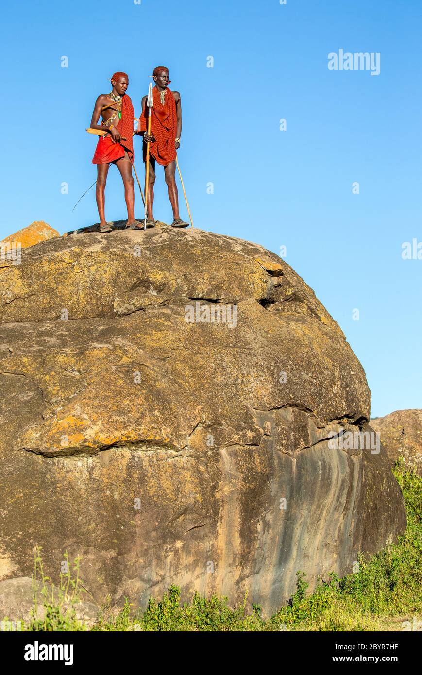 Deux jeunes guerriers Masai sont debout sur une grande pierre en vêtements traditionnels avec une lance contre un ciel bleu. Tanzanie, Afrique de l'est, 12 août 2018. Banque D'Images