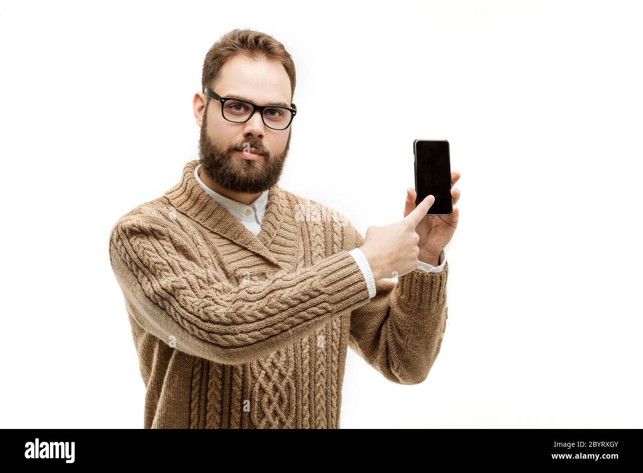 gros plan portrait d'un beau homme avec une belle barbe portant des lunettes et un pull marron chaud. Le modèle pointe l'index sur l'écran tactile de son Banque D'Images