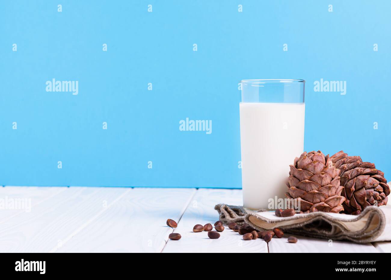 lait sans lactose concept, verre avec lait de cèdre, cônes et noix sur une table blanche sur fond bleu Banque D'Images