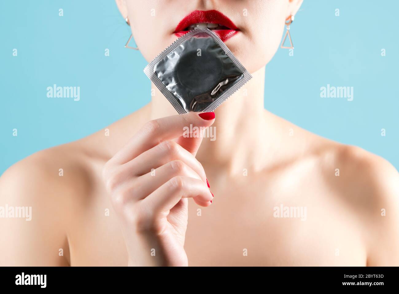 Gros plan sur les lèvres de la fille avec un rouge à lèvres et un condom dans un emballage doré Banque D'Images
