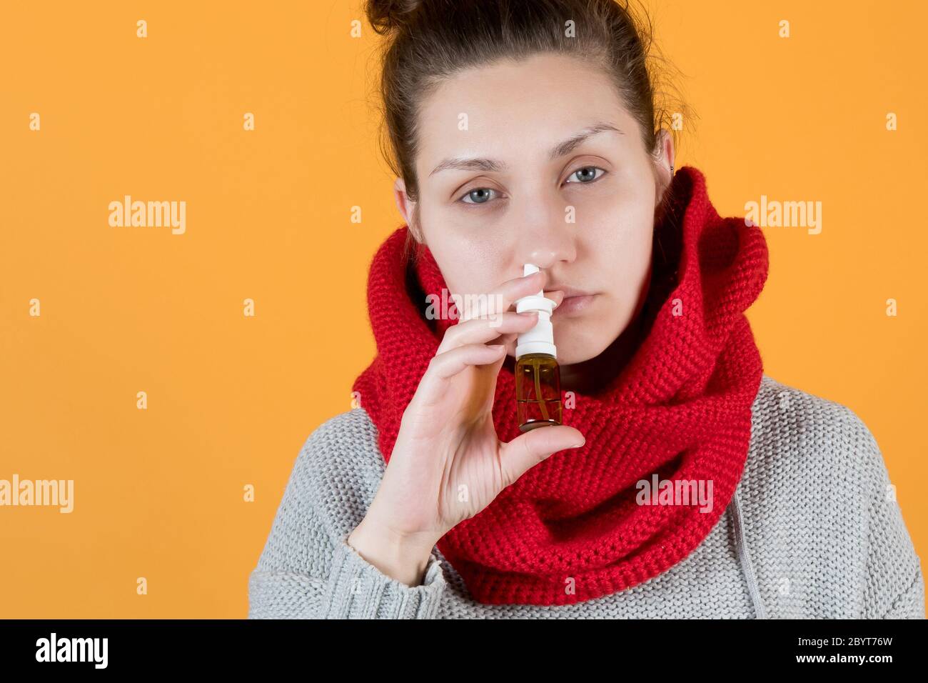 Une jeune femme d'un aspect malade vaporise un traitement pour le rhume et la grippe dans son nez. Banque D'Images