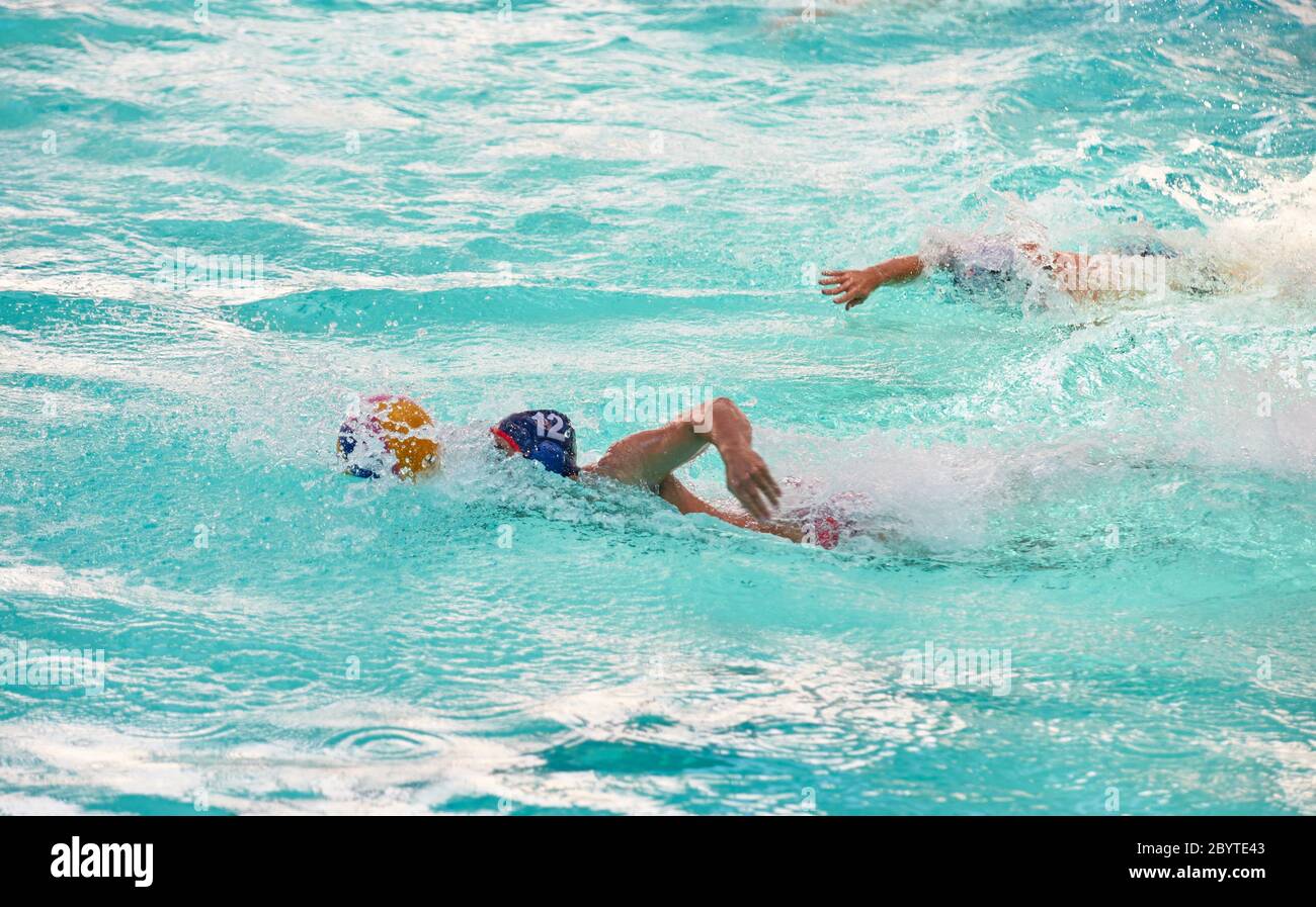 Un joueur de water-polo nageant dans une piscine après une balle jaune éclaboussant de l'eau Banque D'Images