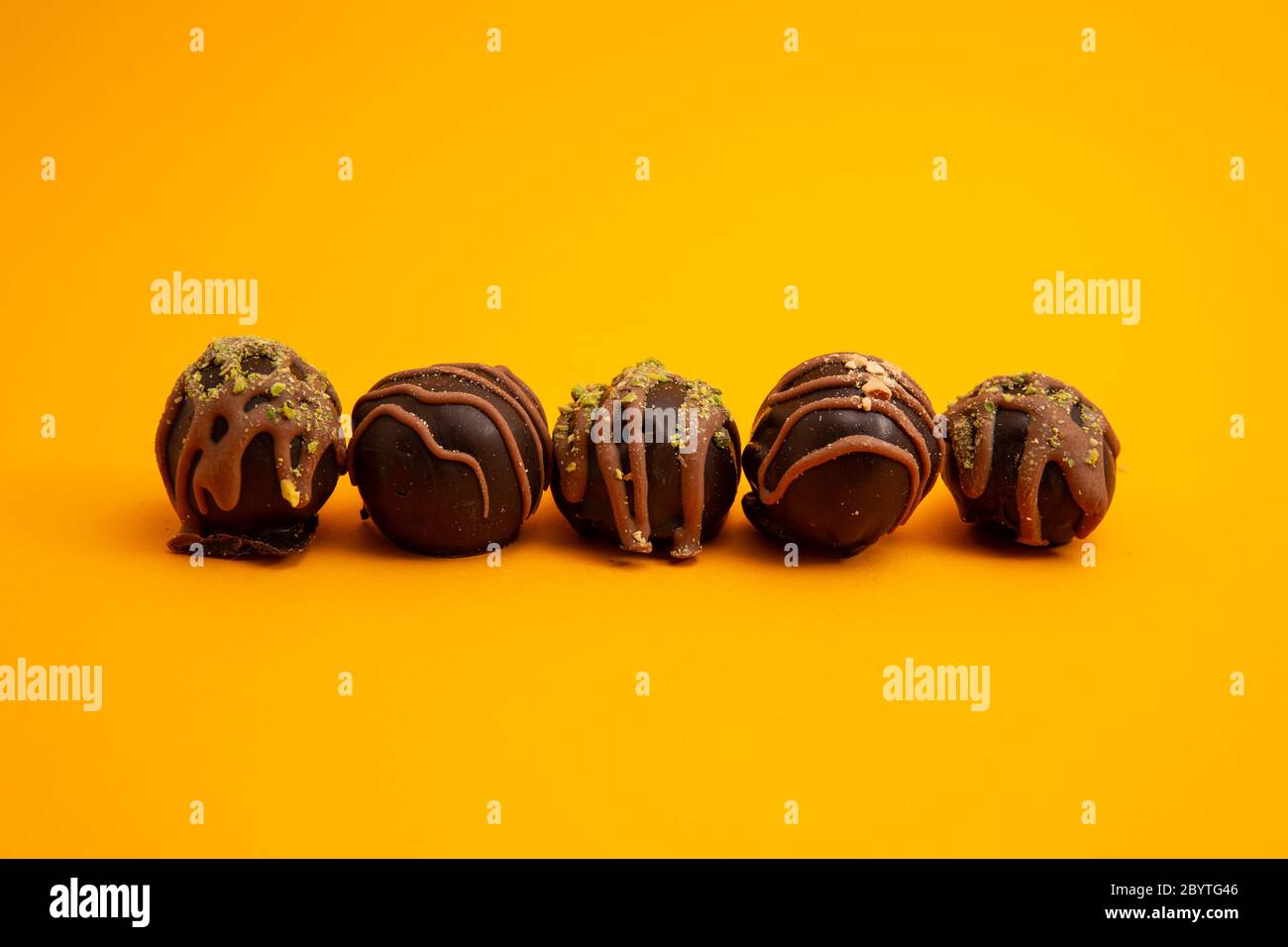 Chocolats ronds doublés avec noix et pistaches isolés sur fond jaune avec espace de copie Banque D'Images