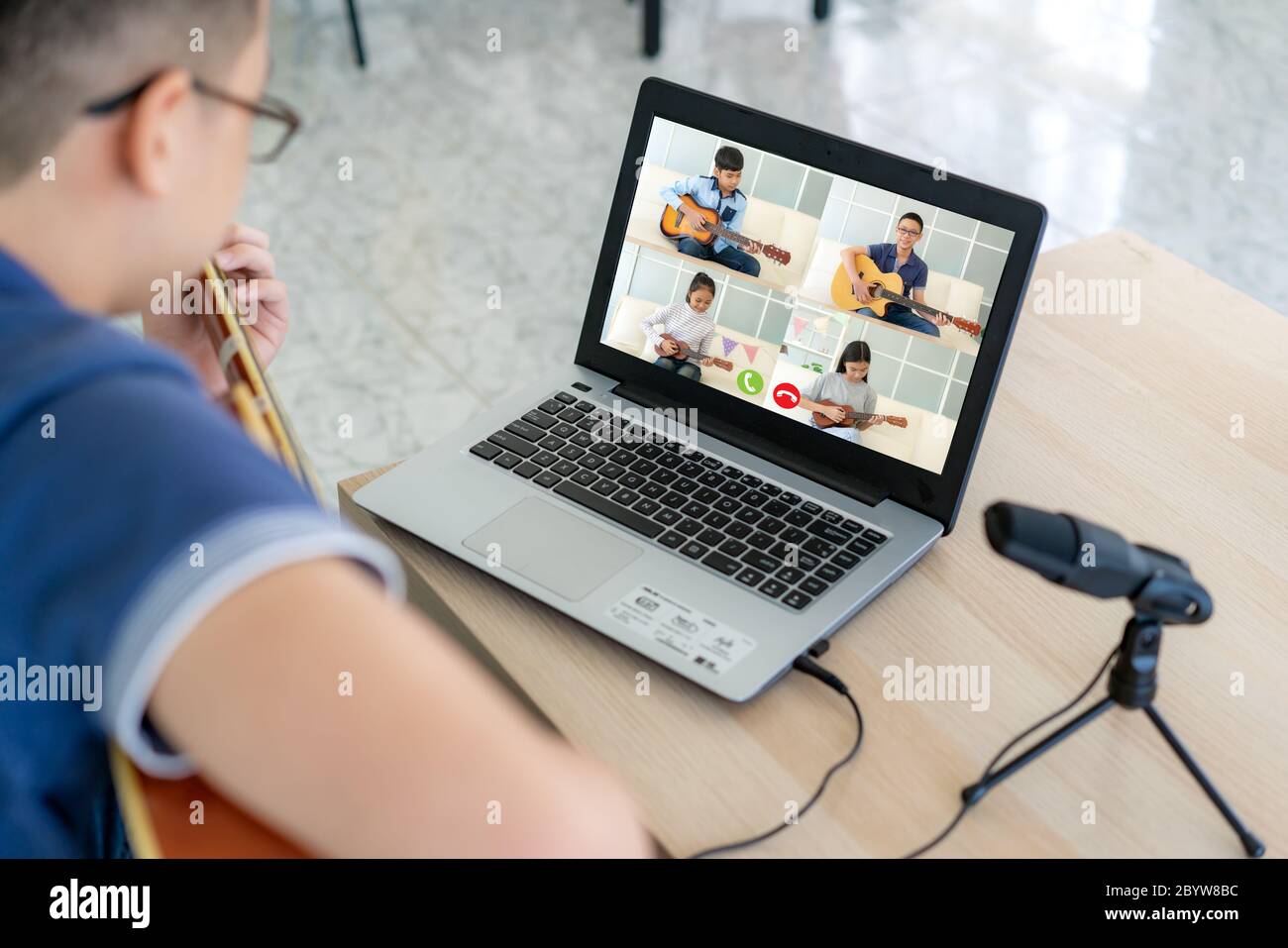 Asiatique garçon jouant de la guitare acoustique Virtual happy hour réunion pour jouer de la musique en ligne avec un ami en vidéo conférence avec ordinateur portable pour un m en ligne Banque D'Images