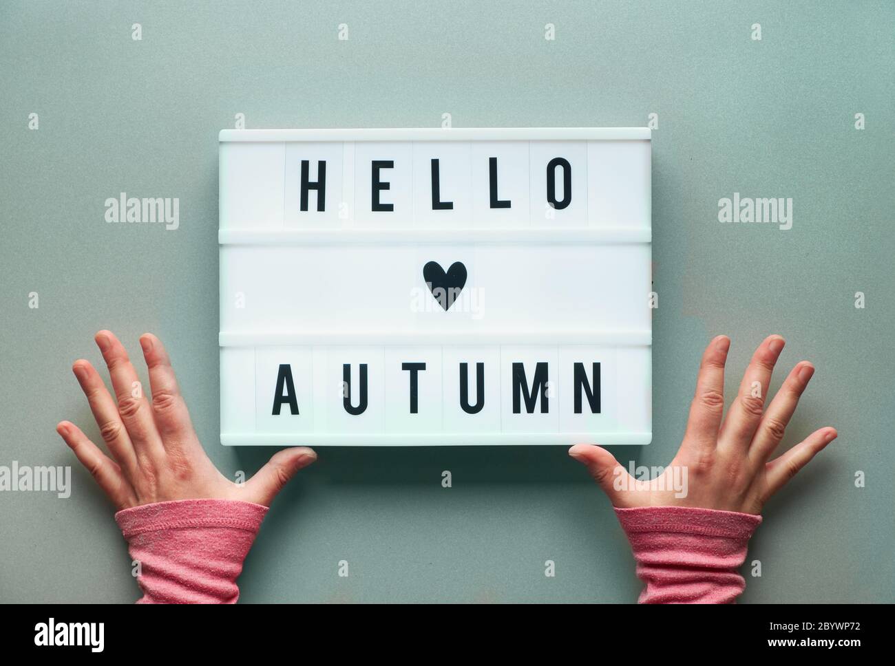Visionneuse avec texte Hello Autumn et coeur dans les mains des femmes. Arrière-plan en papier gris argenté, vue du dessus. Banque D'Images
