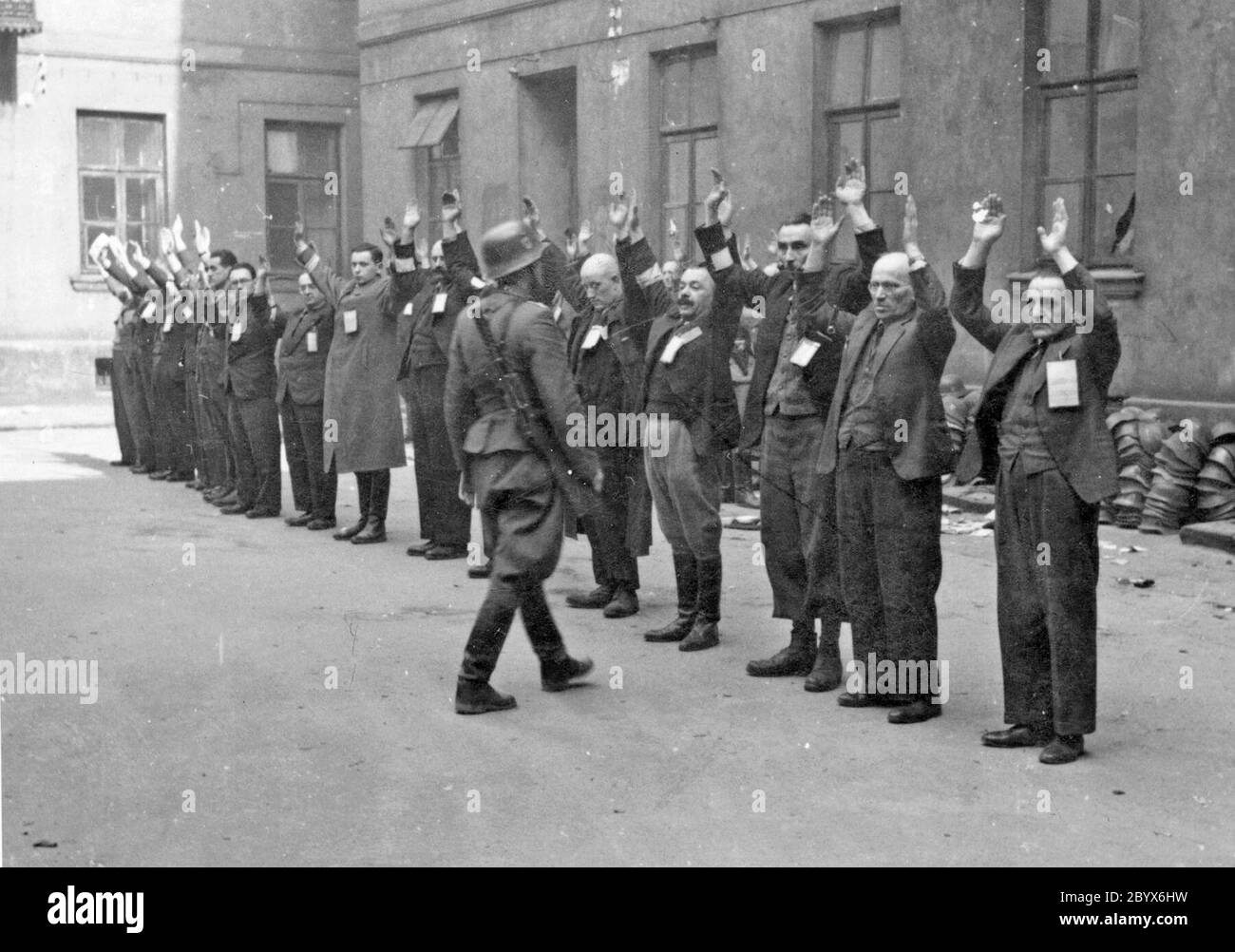 Soulèvement du ghetto de Varsovie: Photographie des troupes SS arrêtant les chefs de département juifs de l'usine de casques Brauer ca. 24 avril 1943. Le "hop" Brauer, de Herman Brouer, a fabriqué des casques pour l'armée allemande, était situé à la rue Nalewki 28-38 et employait 2 mille personnes.[3] leurs travailleurs étaient probablement des derniers Juifs à être déportés du ghetto. Avec le déclenchement du soulèvement le 19 avril 1943, Hermann Brauer a promis aux directeurs de travail juifs qui n'avaient pas été cachés, que l'usine continuerait à fonctionner et leur a demandé de venir travailler. Ces gestionnaires ont reçu des tra spéciaux Banque D'Images