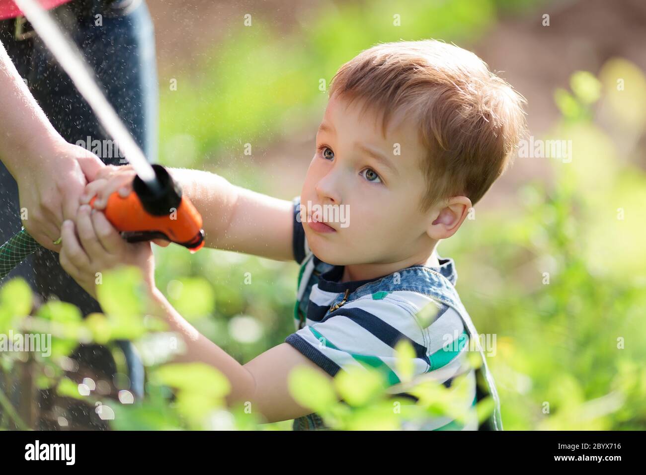 Petit garçon jouant avec un jet d'eau dans un jardin Banque D'Images