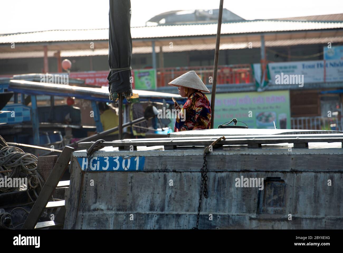 Une femme utilise son téléphone tout en portant un chapeau conique vietnamien (non la) sur son bateau sur le fleuve Hau à CAN Tho, région du delta du Mékong, sud du Vietnam. Banque D'Images