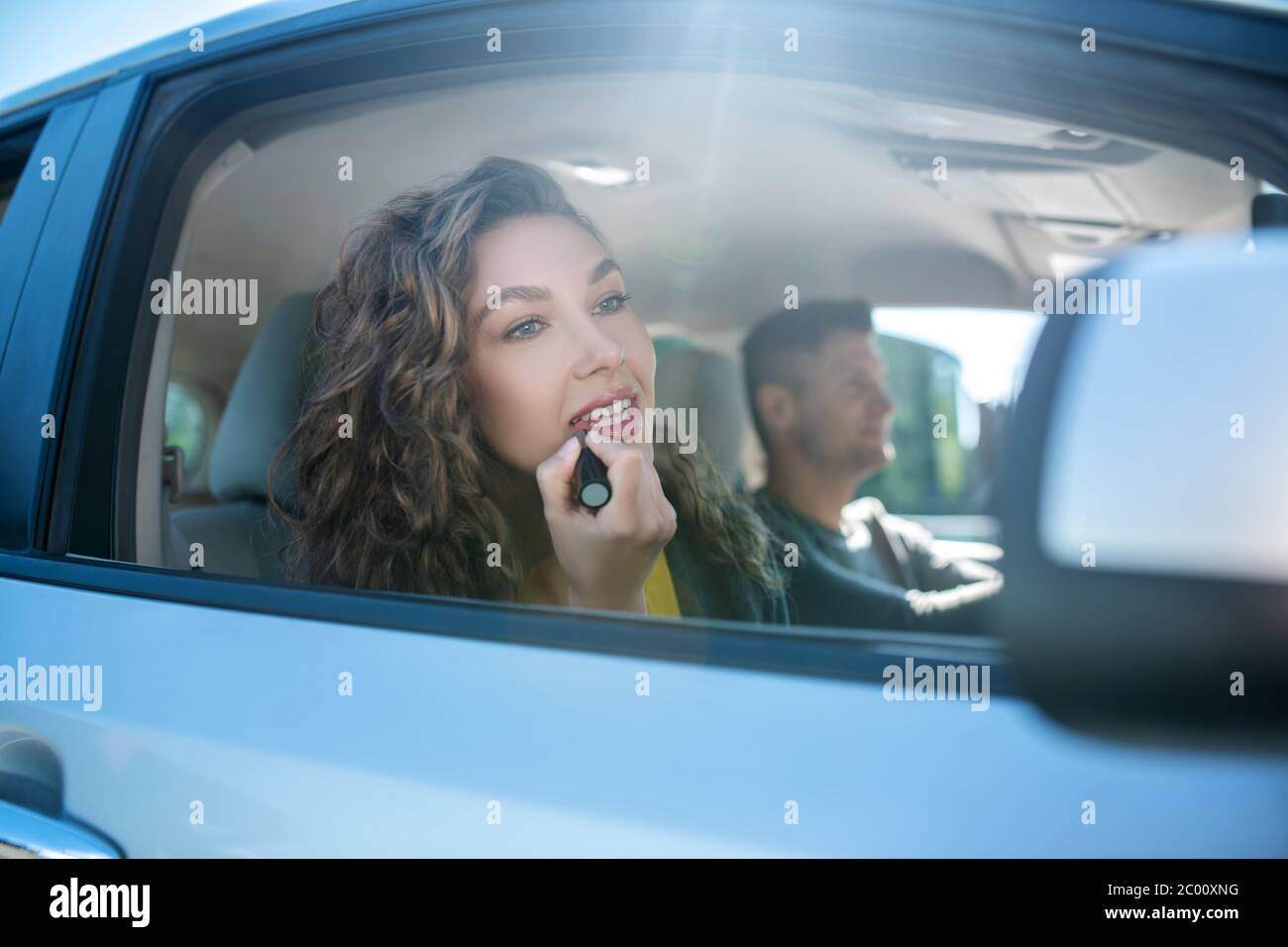 Belle femme peinture des lèvres en voiture regardant dans le miroir latéral Banque D'Images