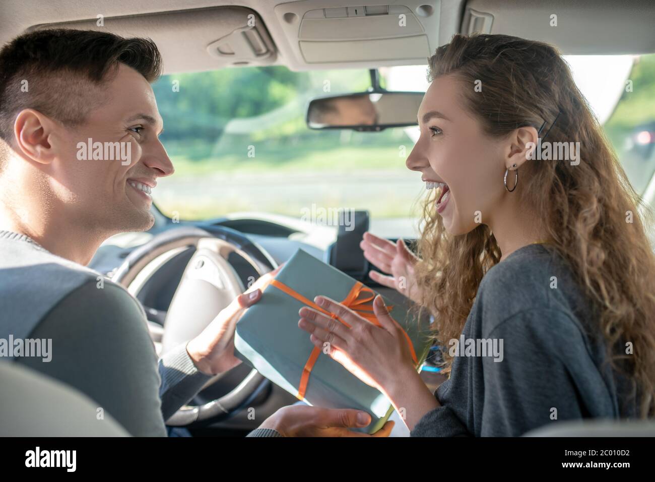 Homme souriant donnant une boîte à une femme joyeuse en voiture Banque D'Images