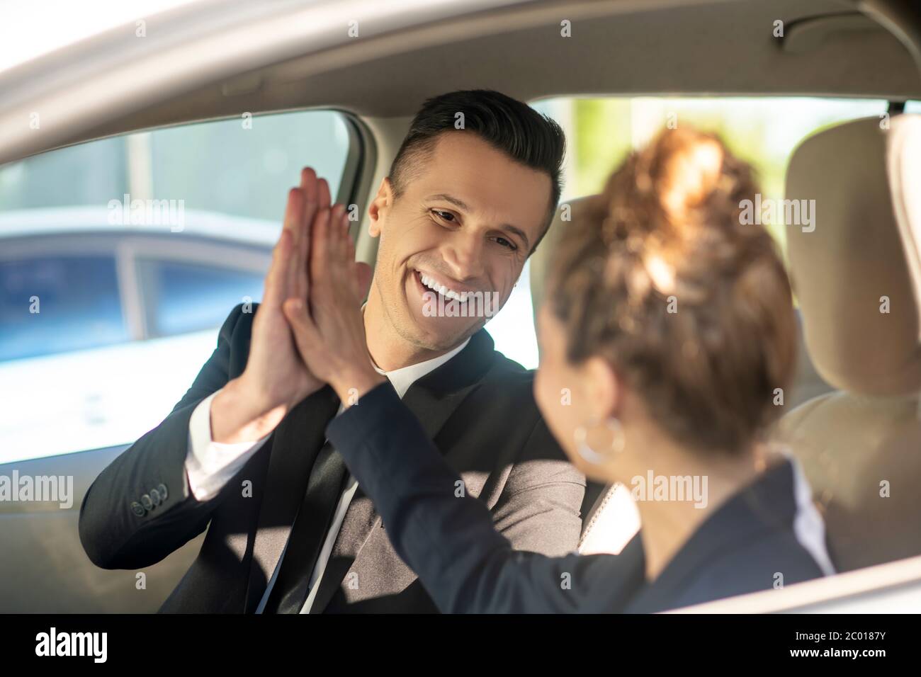 Homme et femme souriants touchant les paumes dans une voiture Banque D'Images