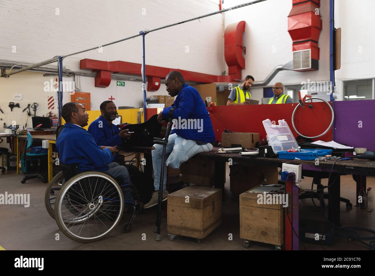 Travailleurs de courses multiples créant des fauteuils roulants dans wharehouse Banque D'Images
