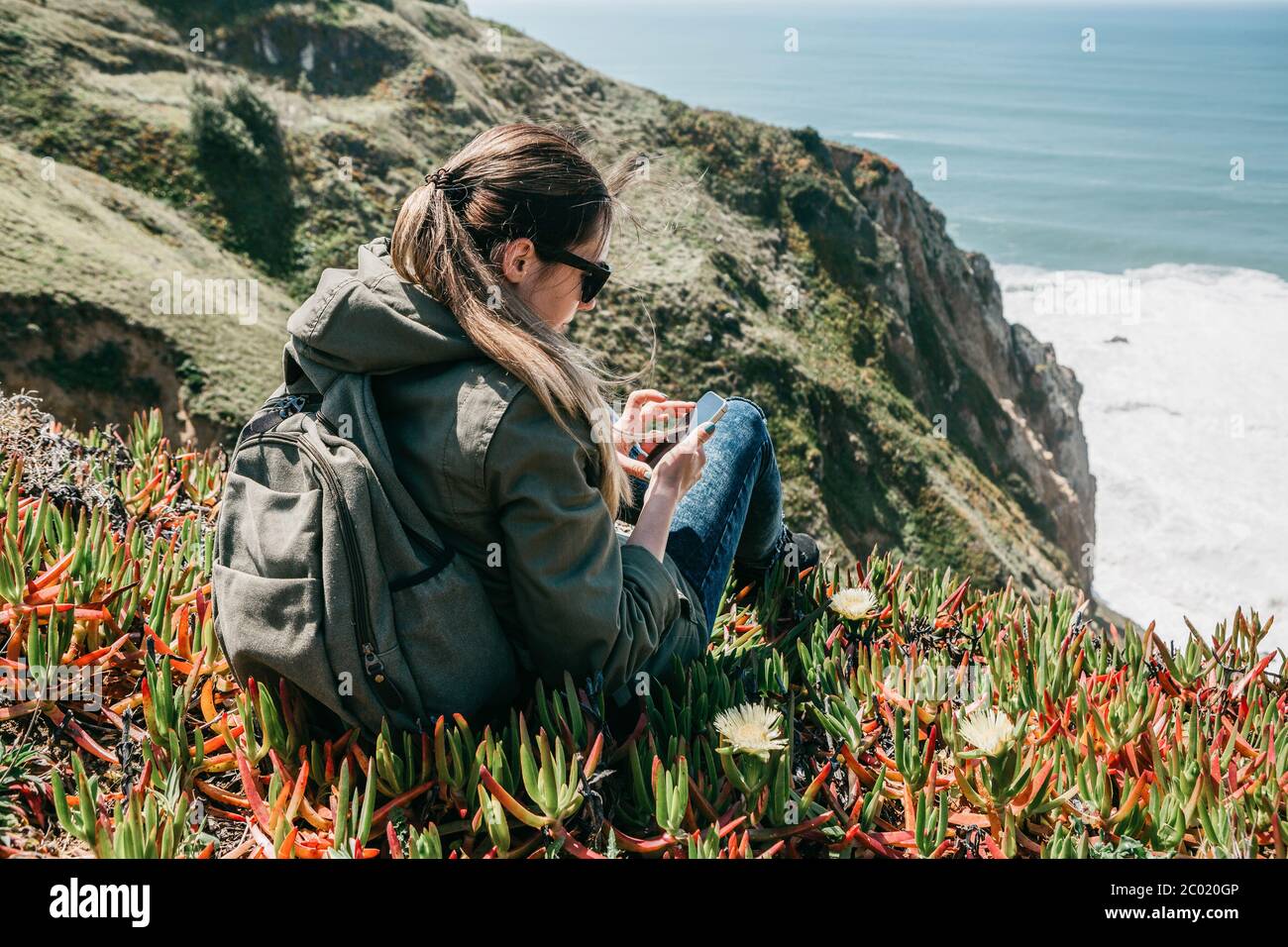 Une jeune fille étudiante ou touriste en solitude utilise un téléphone cellulaire ou mobile pour envoyer un message ou pour passer un appel, ou elle est en ligne sur Internet. Banque D'Images