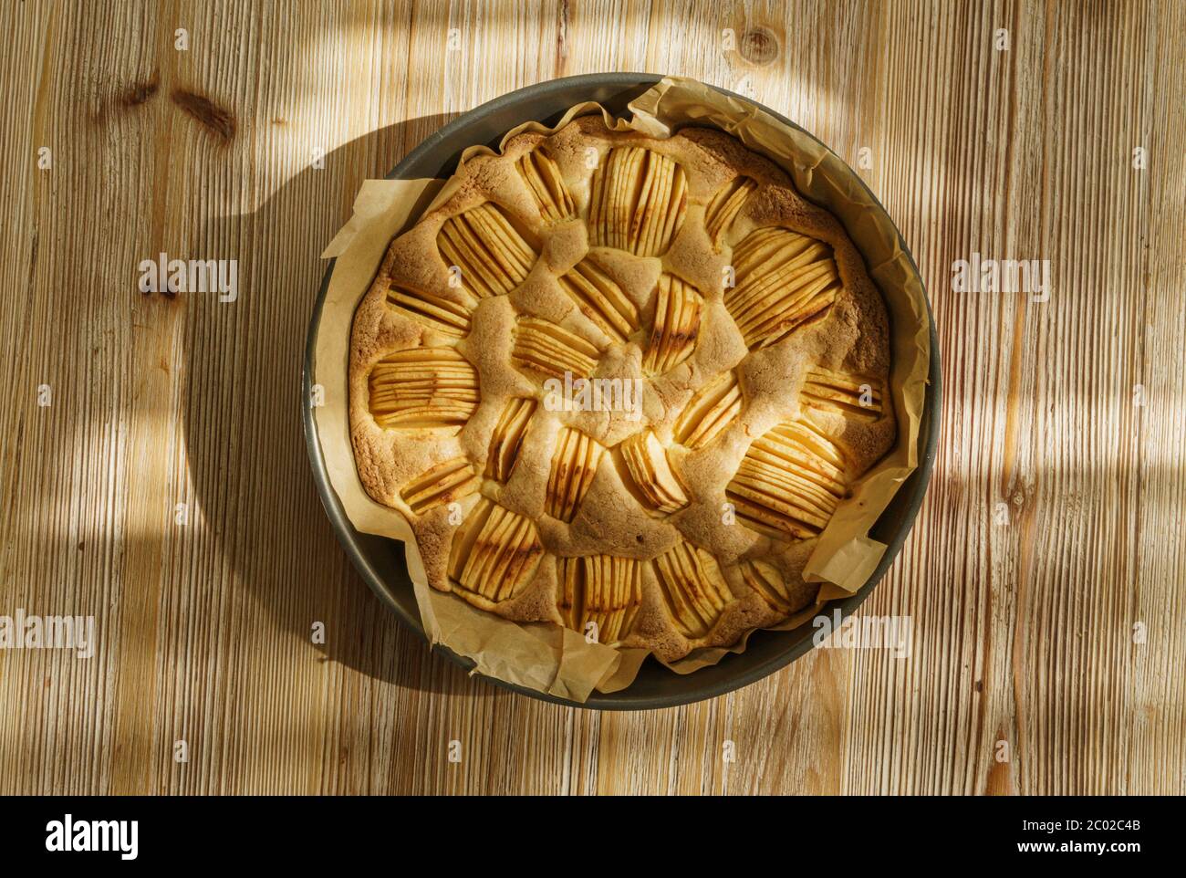 Tarte aux pommes ronde, fraîche du four, sur un panneau en bois, aux tons chauds et à la texture. Banque D'Images