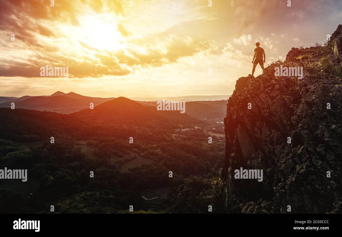 Voyagez seul avec un homme touristique sur les montagnes de la falaise et en regardant la vallée. Silhouette de la personne sur le rocher au coucher du soleil. Randonnée Banque D'Images