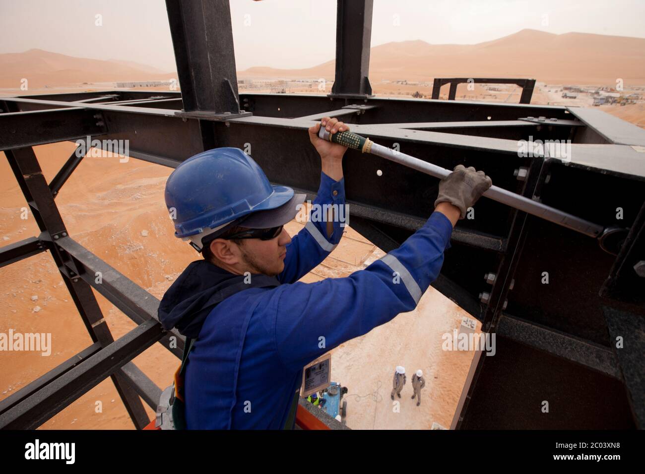 Un ingénieur serre les boulons sur un cadre qu'il construit pour transporter des tuyaux dans une grande installation pétrolière construite dans le désert du Sahara. Banque D'Images