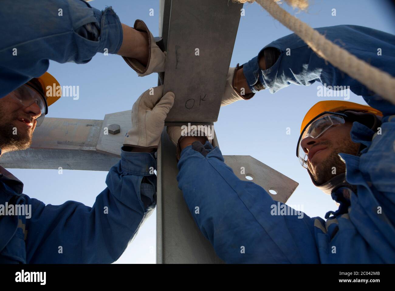 Les ingénieurs serrent les boulons d'un cadre en cours de construction pour transporter les câbles de commande électrique dans une grande installation pétrolière construite dans le désert du Sahara. Banque D'Images