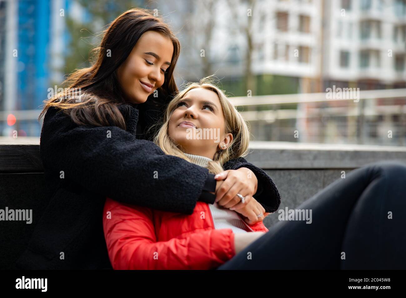 Smiling Meilleurs amis embrassant et assis sur le sol en ville Banque D'Images