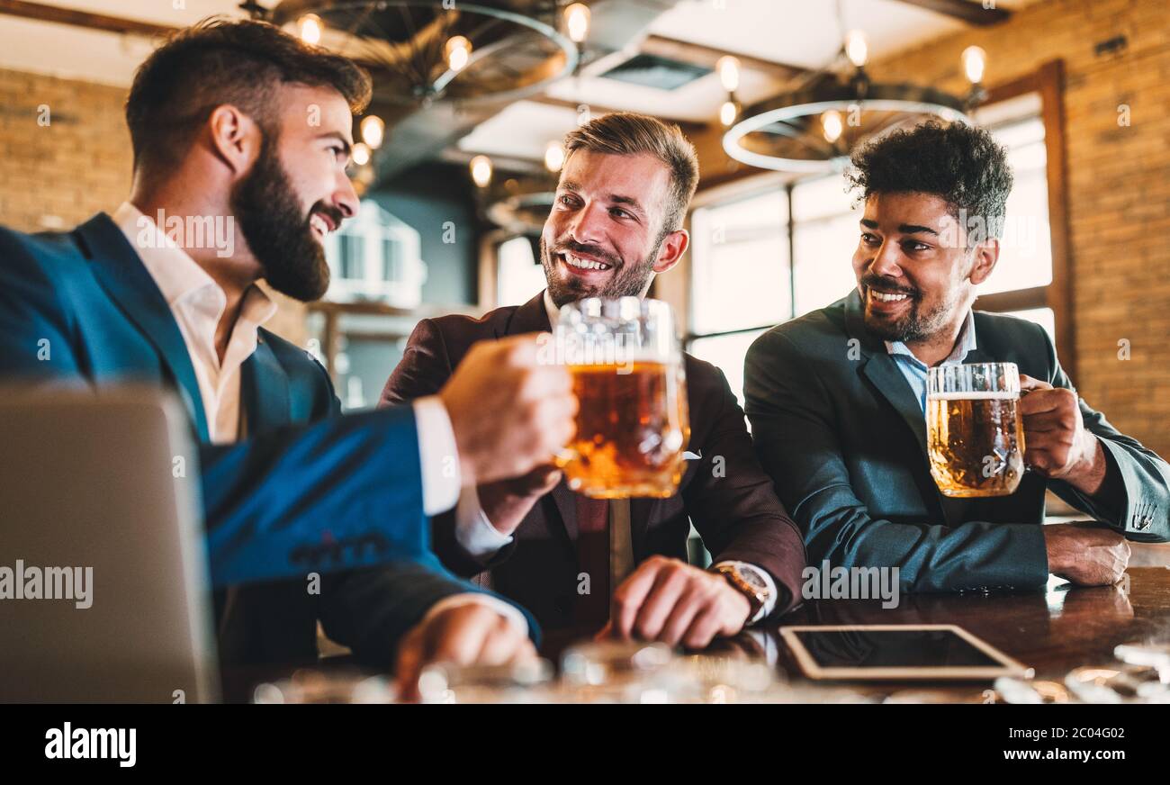 Les hommes d'affaires sont en train de boire de la bière, de parler et de sourire tout en se reposant au pub Banque D'Images