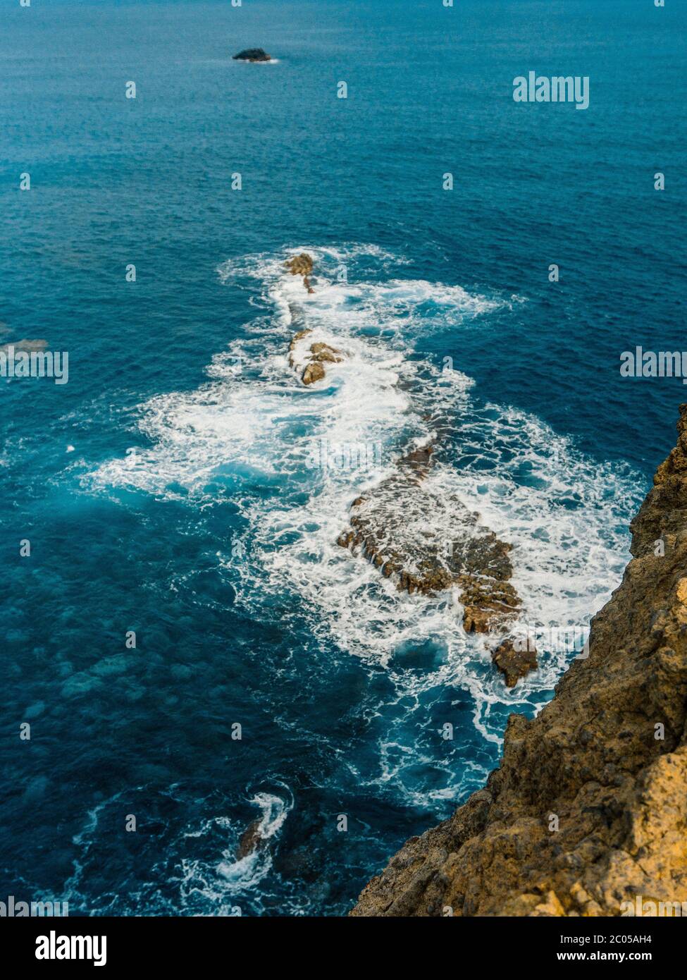 Danger : une vague de mer s'écrasera sur la côte rocheuse avec du spray et de la mousse. Une vague bleue et magnifique se défait contre une falaise Banque D'Images
