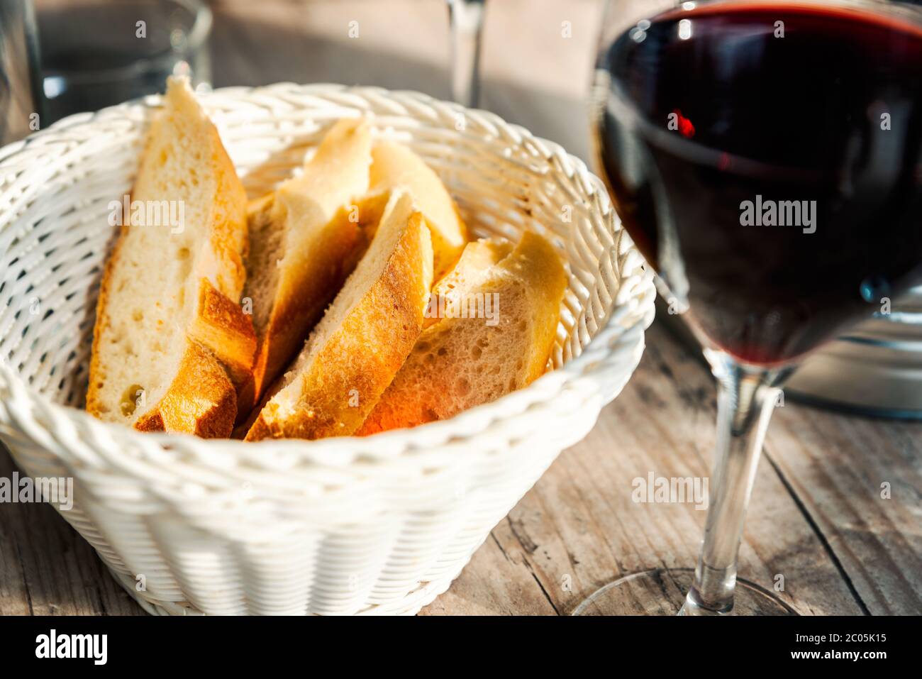 Tranches de baguette dans un panier en osier blanc et un verre de vin rouge sur une table en bois sur une terrasse de café français Banque D'Images