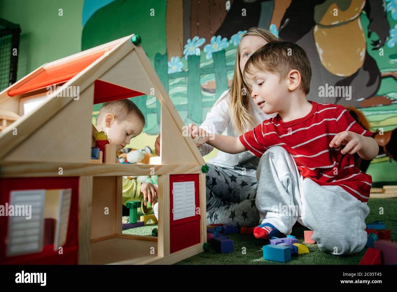 Enfants jouant avec une maison de poupée en bois dans un centre de jeux Banque D'Images