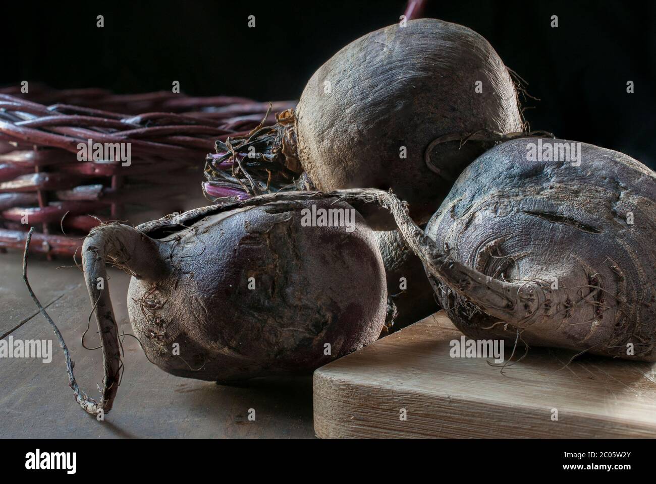 Betteraves sur une planche à découper en bois et un panier au fond avec un fond noir et un rebord léger, concept de légumes biologiques sur une table Banque D'Images