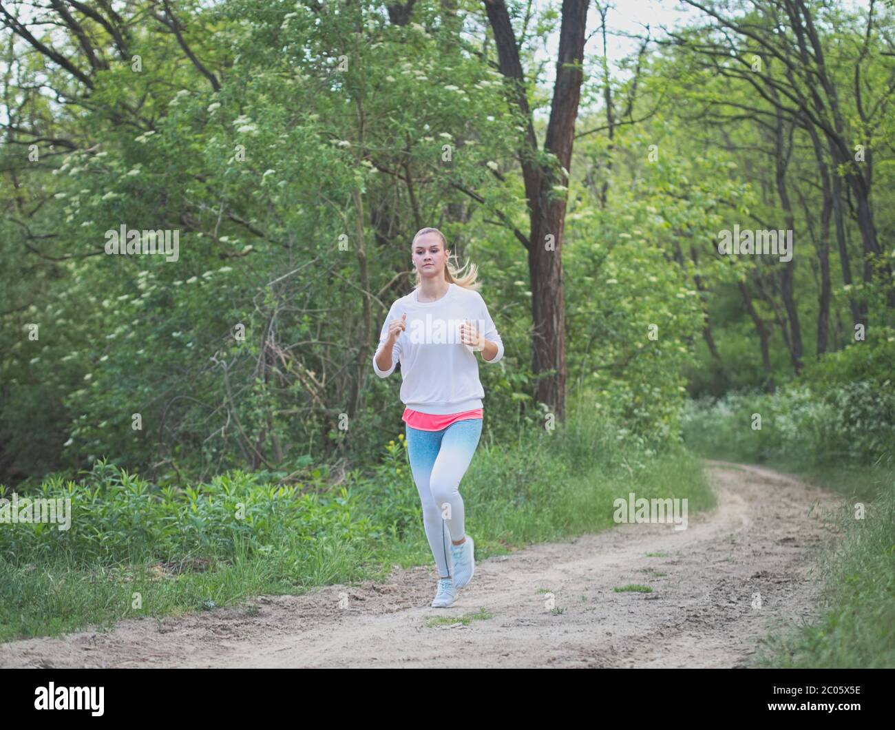 Jeune femme blanche Blonde courant dans la forêt sur une route de terre Banque D'Images