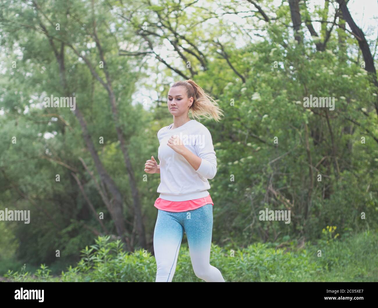 Jeune femme blanche Blonde courant dans la forêt sur une route de terre Banque D'Images