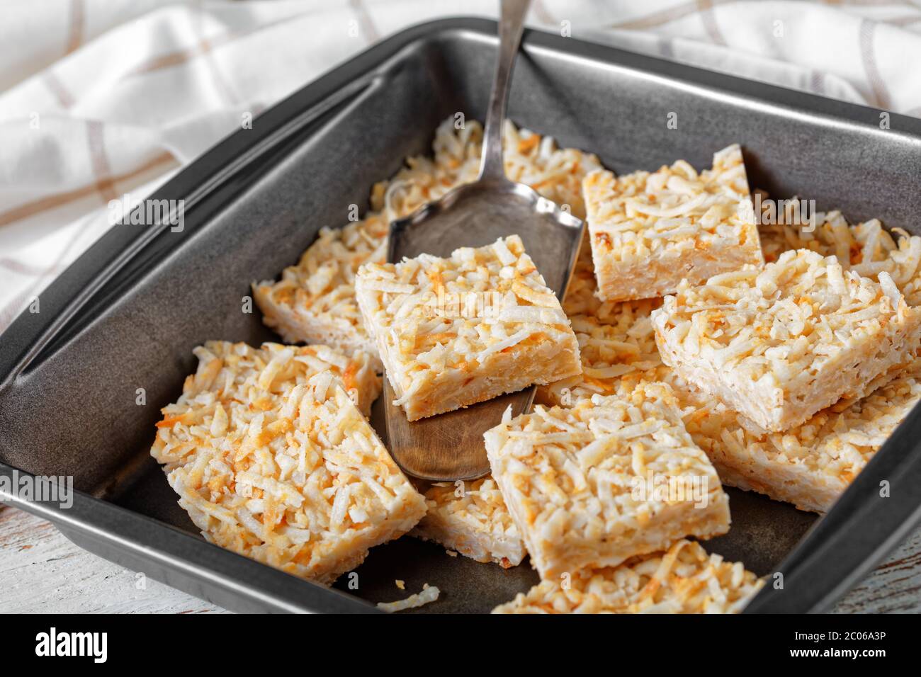 barres de crack à la noix de coco sans cuisson dans un plat de cuisson sur une table rustique en bois avec une serviette de cuisine, recette sans sucre végétalien, vue horizontale d'en haut, proche- Banque D'Images