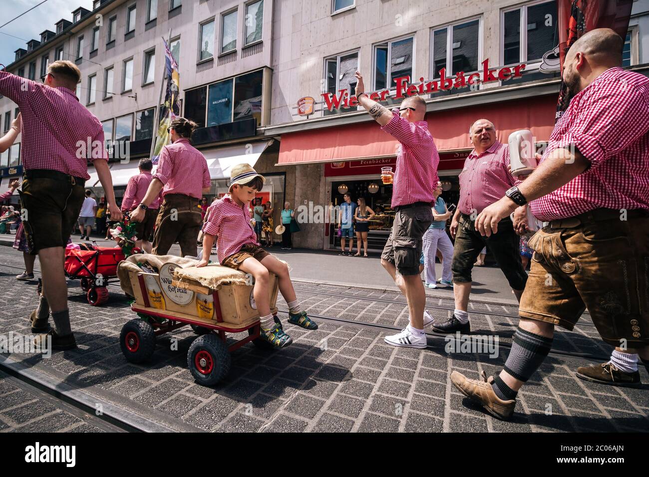 Un groupe d'hommes en costume traditionnel tire un jeune garçon mignon avec un petit chariot de la brasserie locale, Würzburger Hofbräu au défilé de Kiliani. Banque D'Images