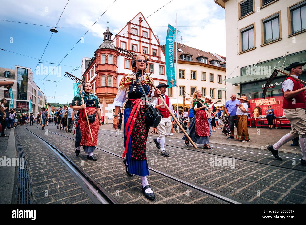 Des personnes présentant les tenues traditionnelles colorées et portant des outils de récolte typiques au défilé d'ouverture du festival d'été de Kiliani en Bavière. Banque D'Images