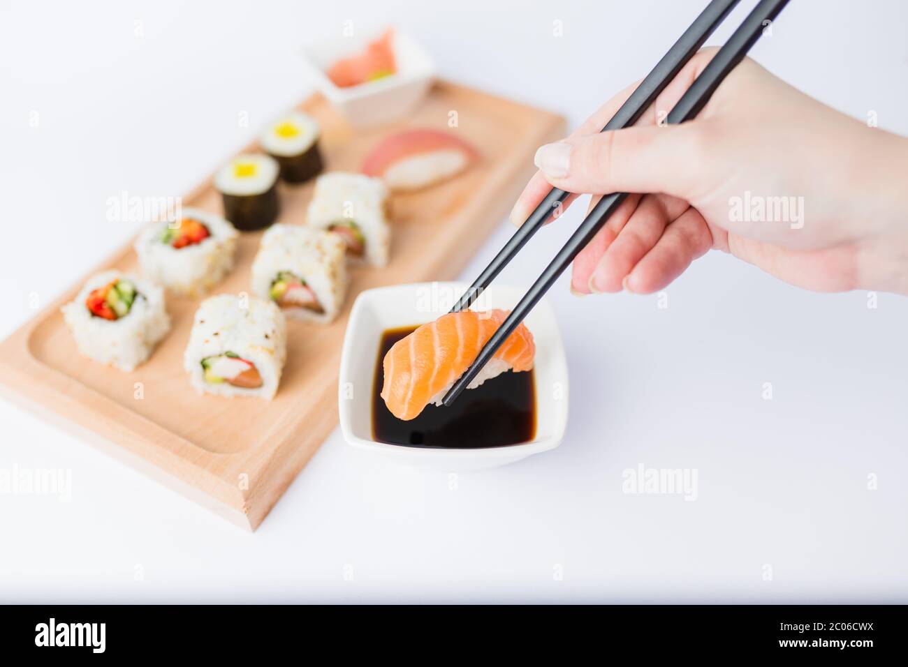 Gros plan de la femme tenant des baguettes avec un rouleau de sushi au saumon et un bol avec sauce soja sur la table, portion de repas japonais traditionnel en arrière-plan. Banque D'Images