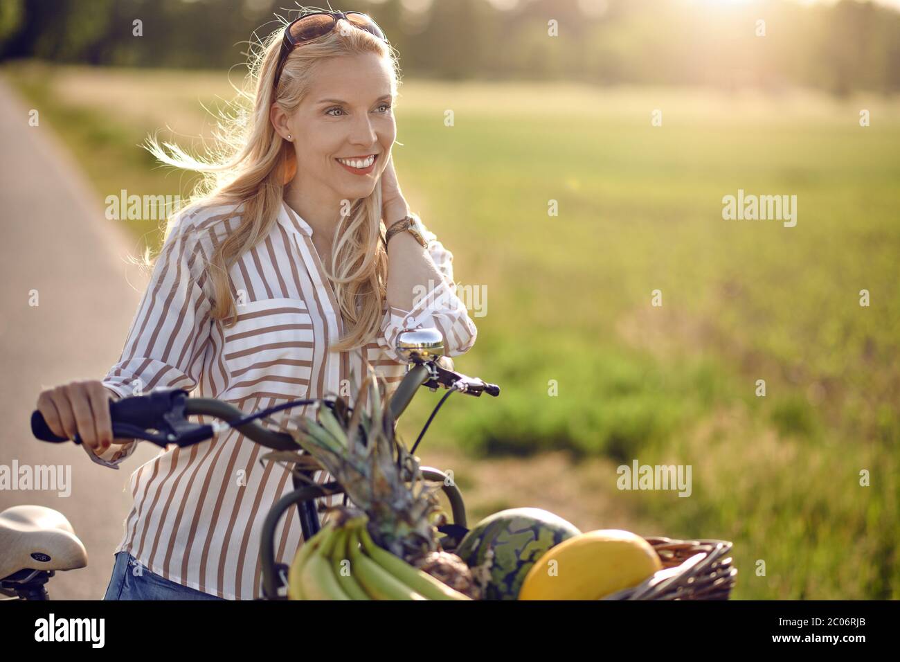 Femme utilisant son vélo pour acheter des produits frais debout sur une route rurale rétroéclairé par une lueur chaude du soleil souriant heureux à la caméra comme elle la tient Banque D'Images