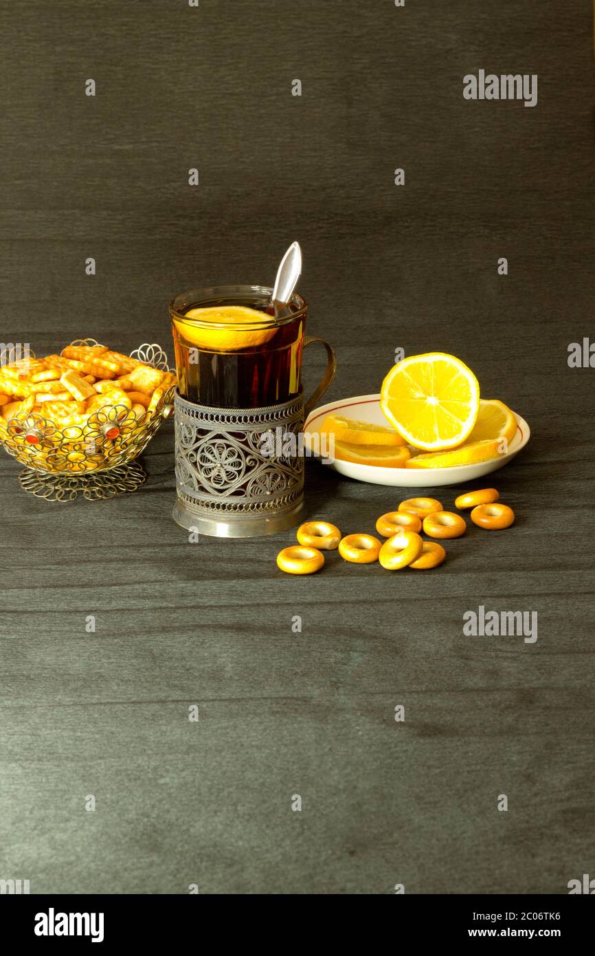 Thé dans un porte-gobelet argenté avec citron et bagels sur fond noir Banque D'Images