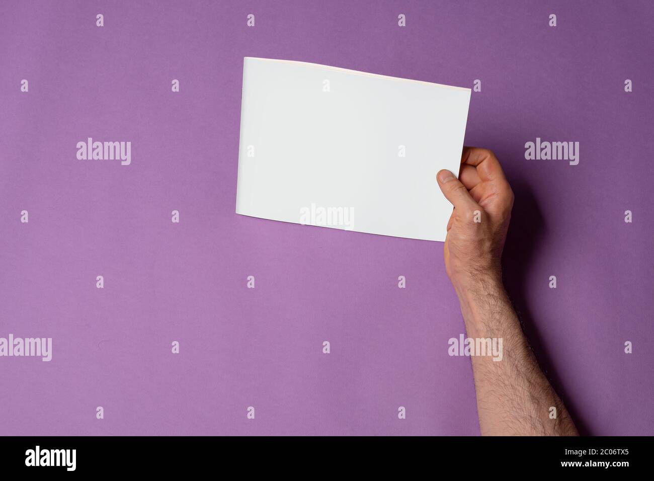 Main droite mâle tenant un catalogue avec couverture vierge sur fond violet, modèle de série maquette prêt pour votre conception, chemin de sélection inclus Banque D'Images