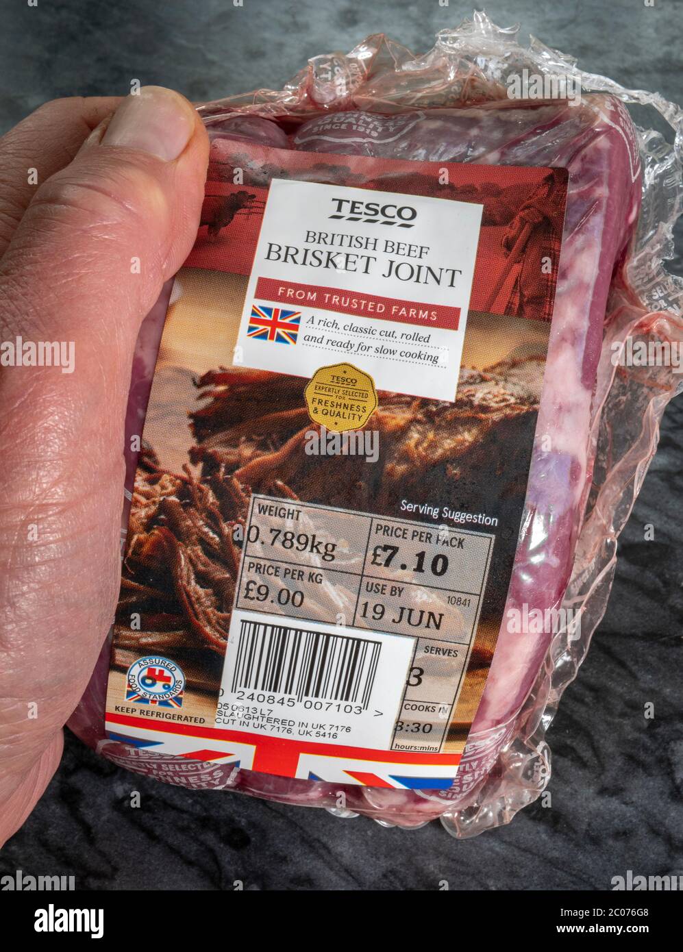 Gros plan de la main d’un homme tenant un joint de poitrine de bœuf britannique Tesco frais, non cuit / cru, dans un emballage en plastique portant une étiquette d’information de supermarché. Banque D'Images
