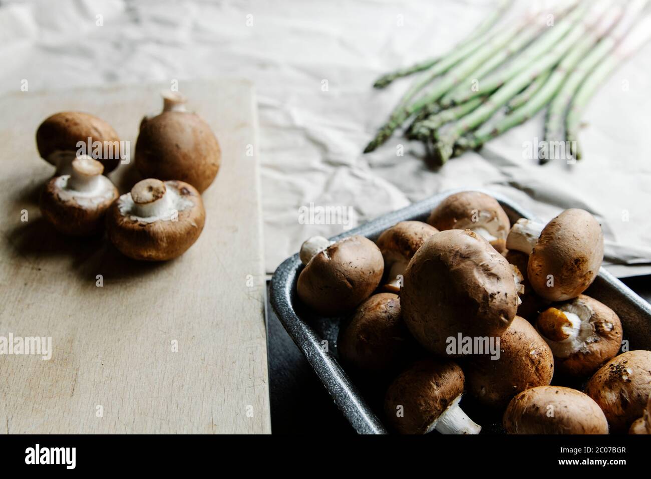 Pile de champignons bruns à angle élevé sur table en bois et tiges d'asperges vertes sur papier Banque D'Images