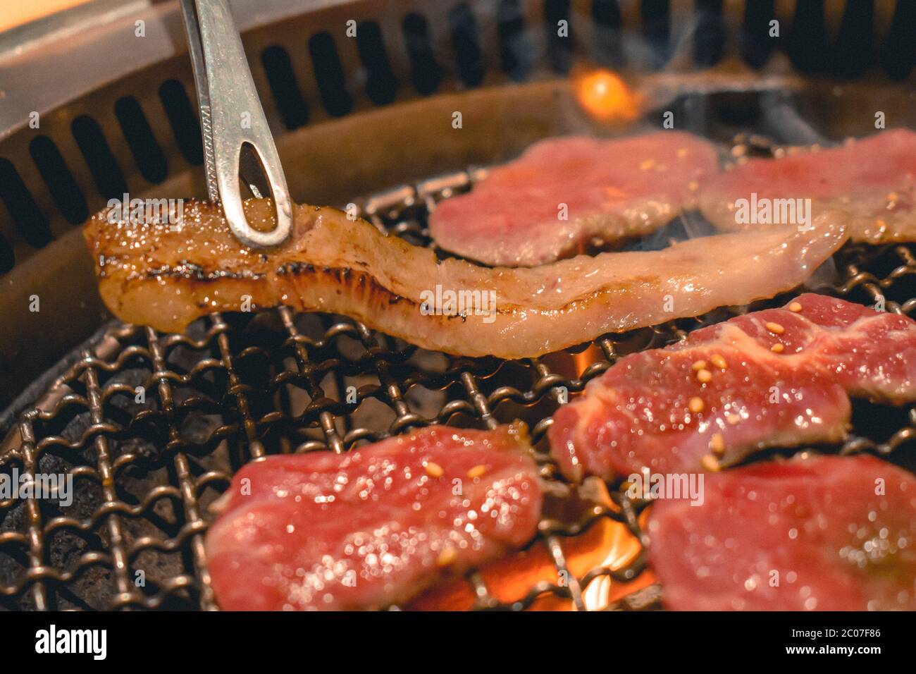 Pincettes ramassant un morceau de poitrine bien faite d'un gril avec des morceaux de délicieux bœuf Banque D'Images