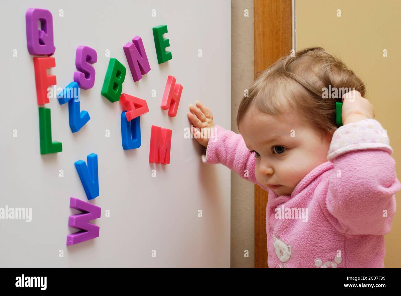 Développement de la petite enfance. Une fille d'un an jouant avec des lettres magnétiques de réfrigérateur. Banque D'Images