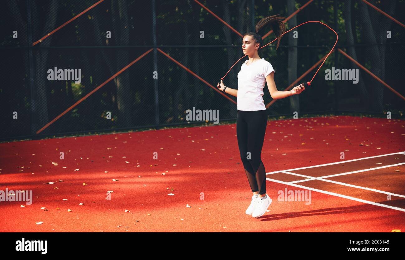 Jeune fille sportive de race blanche utilisant une corde à sauter sur un stade de tennis rouge dans un matin ensoleillé d'été Banque D'Images