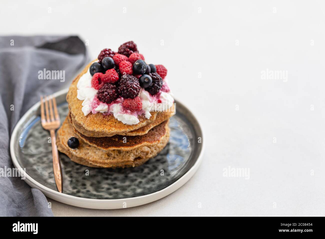 Image horizontale de crêpes de flocons d'avoine recouvertes de yaourt et de baies, servies sur une assiette en céramique grise. Espace négatif. Banque D'Images