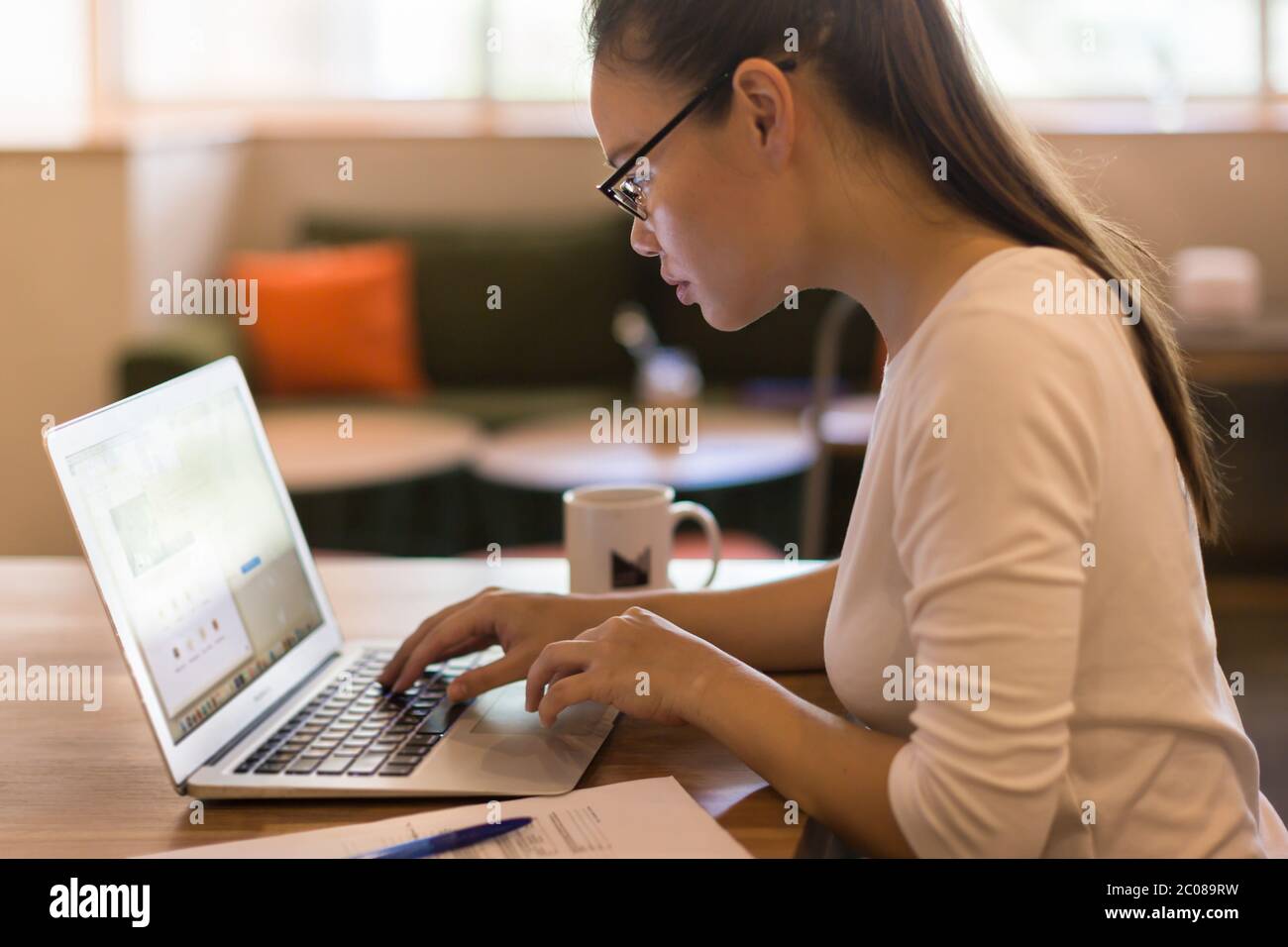 Femme d'affaires tapant sur son ordinateur portable avec des documents et un stylo sur son bureau Banque D'Images
