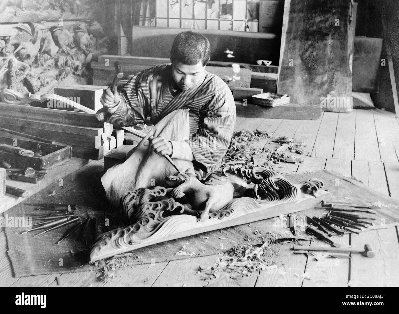 [ 1910s Japon - Dragon de bois de sculpture ] — UN artisan en vêtements traditionnels est en train de sculpter un dragon de bois. Il est entouré de ses outils et de ses morceaux de bois. imprimé argent gélatine vintage du xxe siècle. Banque D'Images