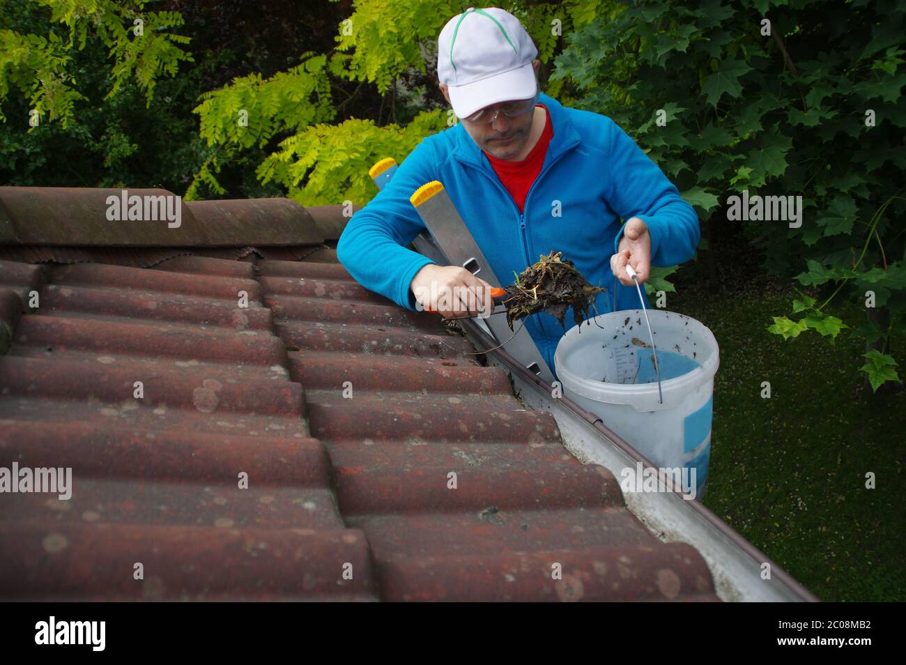 Homme sur l'échelle nettoie la gouttière sur le toit. Entretien d'une maison privée. Banque D'Images